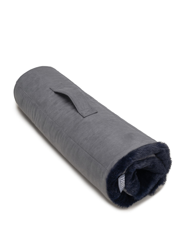 Cama para perro enrollable Brott en color azul marino y gris, enrollada con asa para fácil transporte.